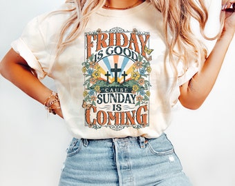 May include: A cream-colored t-shirt with a vintage-style graphic that reads "Friday is good 'cause Sunday is coming". The graphic features a floral design, crosses, and a sunburst.