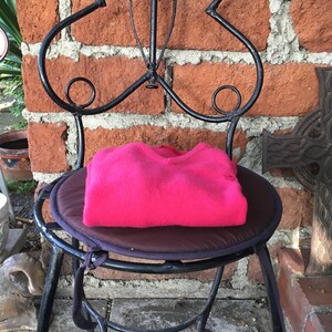 May include: A pink sweater folded and placed on a black metal chair with a brown cushion. The chair is in front of a brick wall.