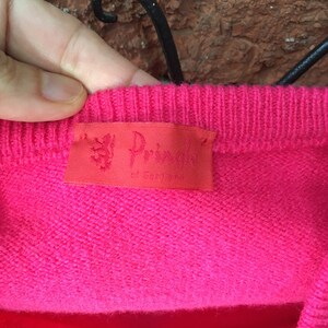 May include: A pink knitted sweater with a red label that reads "The Pringle of Scotland".