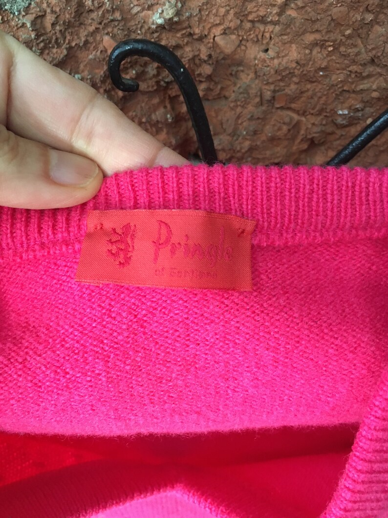 May include: A pink knitted sweater with a red label that reads "The Pringle of Scotland".