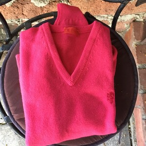 May include: A pink v-neck sweater with a small embroidered logo on the right side.