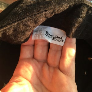 Op de afbeelding: Zwarte baseballpet met een wit label met de tekst "Disneyland Resort"