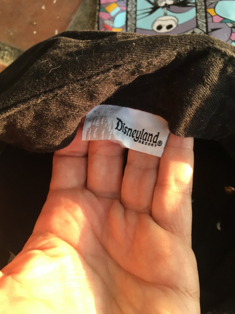 Op de afbeelding: Zwarte baseballpet met een wit label met de tekst "Disneyland Resort"