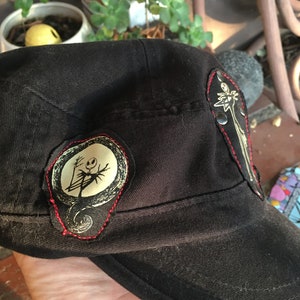 Op de afbeelding: Zwarte baseballpet met twee geborduurde patches met daarop het personage Jack Skellington uit de film The Nightmare Before Christmas.