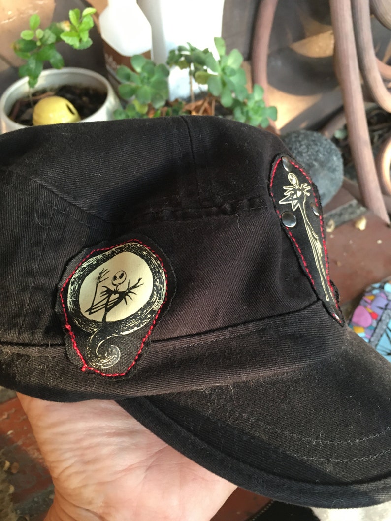 Op de afbeelding: Zwarte baseballpet met twee geborduurde patches met daarop het personage Jack Skellington uit de film The Nightmare Before Christmas.