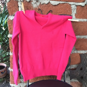 May include: A pink long-sleeved v-neck sweater with a small embroidered logo on the front.