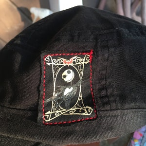 Op de afbeelding: Zwarte baseballpet met een rood gestikt patch met een witte omtrek van Jack Skellington uit The Nightmare Before Christmas.