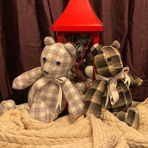 May include: Two plaid teddy bears with white ribbon bows sit in front of a red lantern filled with Christmas ornaments. The bears are made from repurposed fabric.