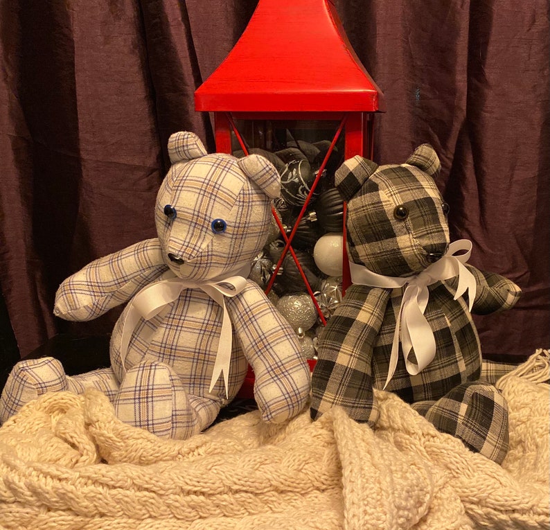 May include: Two plaid teddy bears with white ribbon bows sit in front of a red lantern filled with Christmas ornaments. The bears are made from repurposed fabric.