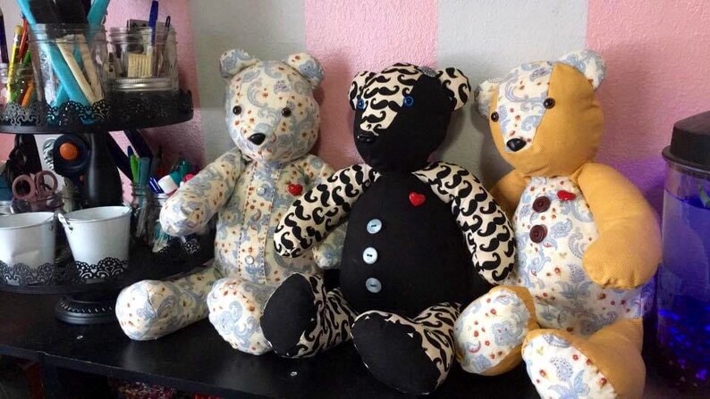 May include: Three teddy bears with different patterns and colors. The bear on the left is white with a blue and white paisley pattern. The bear in the middle is black with a white and black mustache pattern. The bear on the right is yellow with a blue and white paisley pattern.