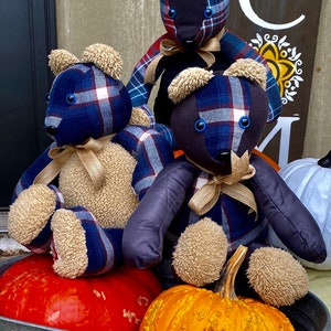 May include: Three plaid teddy bears with blue, red, and white plaid fabric and brown fur accents sit on a metal tub with two pumpkins. One pumpkin is orange and the other is red.