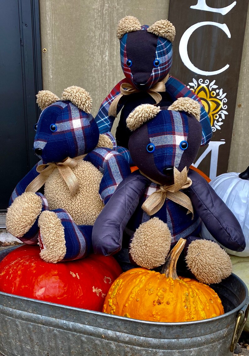 May include: Three plaid teddy bears with blue, red, and white plaid fabric and brown fur accents sit on a metal tub with two pumpkins. One pumpkin is orange and the other is red.