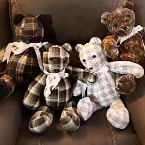 May include: Four plaid teddy bears with white ribbon bows. The bears are sitting on a brown leather chair. The bears are made from different fabrics, including plaid, camouflage, and blue and white checkered fabric.