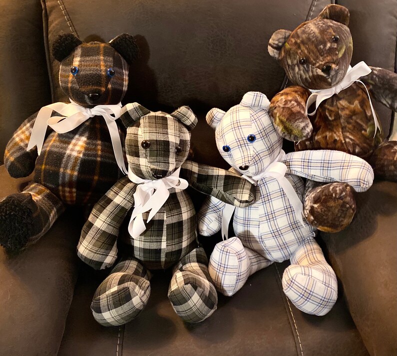 May include: Four plaid teddy bears with white ribbon bows. The bears are sitting on a brown leather chair. The bears are made from different fabrics, including plaid, camouflage, and blue and white checkered fabric.