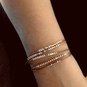 Peut inclure: Un ensemble de quatre bracelets avec des cordons et des perles de différentes couleurs. Les bracelets sont en perles d'argent et d'or et ont un design simple et élégant.