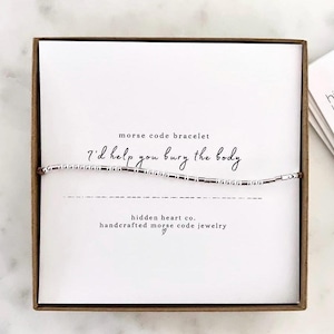 May include: A silver beaded bracelet with the message "I'd help you bury the body" in Morse code. The bracelet is packaged in a white box with the words "hidden heart co. handcrafted morse code jewelry" printed on it.