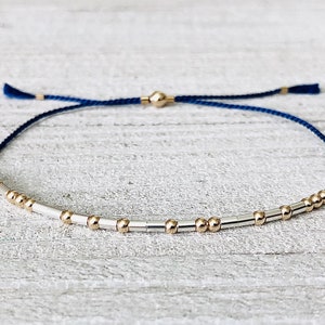 May include: A navy blue string bracelet with silver and gold beads. The bracelet is adjustable and has a tassel on each end.