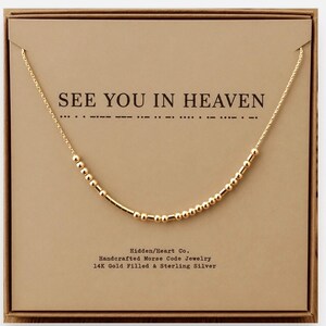 May include: A gold-colored chain necklace featuring a series of small round beads and short cylindrical bars arranged in a Morse code pattern. The necklace is displayed on a tan card printed with the text SEE YOU IN HEAVEN and Hidden/Heart Co.