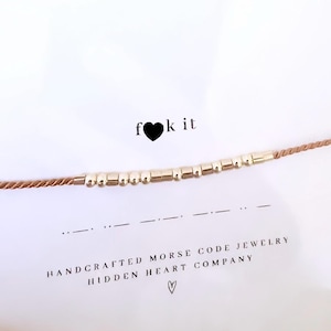 Peut inclure: Un bracelet en cordon marron avec des perles dorées qui épellent "f ♥ k it" en code Morse. Le bracelet est fait à la main et est livré avec une carte qui dit "Bijoux en code Morse faits à la main Hidden Heart Company".