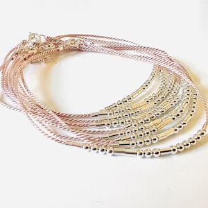 Peut inclure: Un ensemble de dix bracelets délicats en perles roses et argentées. Chaque bracelet présente un design simple avec de petites perles argentées et une perle tubulaire argentée.