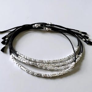 May include: A set of layered bracelets with black cord and silver beads. The bracelets are tied together with a knot at the end.