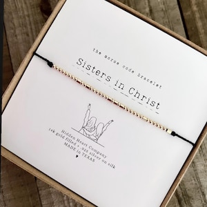 Peut inclure: Un bracelet en argent 925 plaqué or sur un cordon noir avec les mots "Sisters in Christ" en code morse. Le bracelet est emballé dans une boîte blanche avec le logo de Hidden Heart Company et le texte "14k gold filled .925 silver on silk MADE in TEXAS".