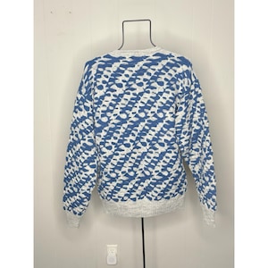 May include: A blue and white patterned sweater. The sweater features a textured design with a crew neck and long sleeves. The cuffs and hem are a light gray color. The sweater is displayed on a black hanger.