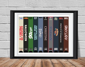 Könnte beinhalten: Ein gerahmter Druck von VHS-Kassetten mit Titeln wie "Sie leben", "Prinz der Dunkelheit", "Starman", "Christine", "Das Ding", "Flucht aus New York", "Der Nebel", "Halloween" und "Assault on Precinct 13".