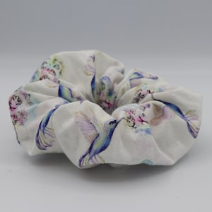 Puede incluir: Scrunchie blanco con estampado de colibrí acuarela. Los colibríes son azules, morados y verdes con flores rosas.
