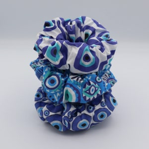 May include: Three blue and white patterned scrunchies with an evil eye design. The scrunchies are stacked on top of each other.