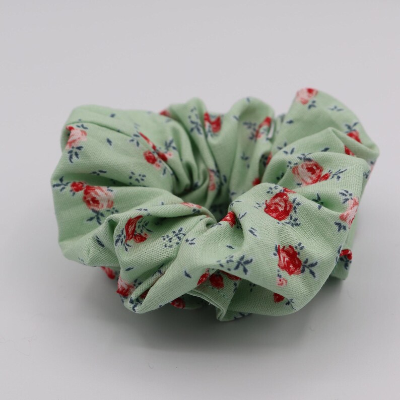 May include: A green scrunchie with a floral pattern featuring red roses and blue leaves.