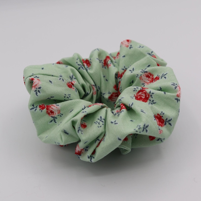May include: A green scrunchie with a floral pattern featuring red roses and green leaves.