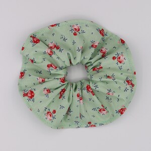May include: A green fabric scrunchie with a floral pattern featuring red roses.