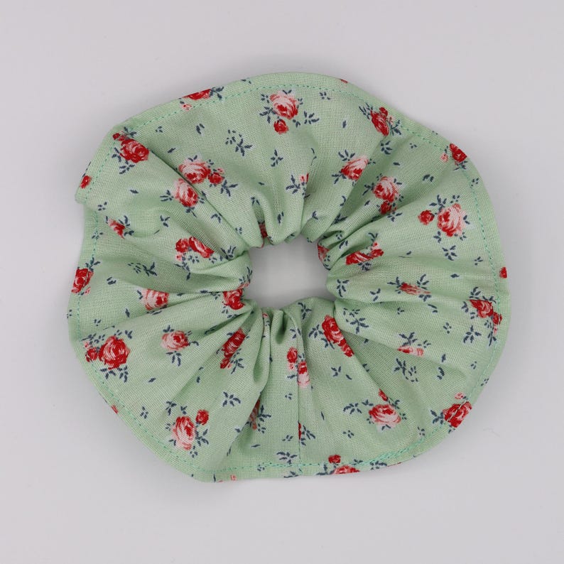 May include: A green fabric scrunchie with a floral pattern featuring red roses.