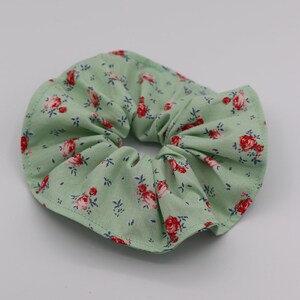 May include: A green fabric scrunchie with a floral pattern featuring red and white roses.