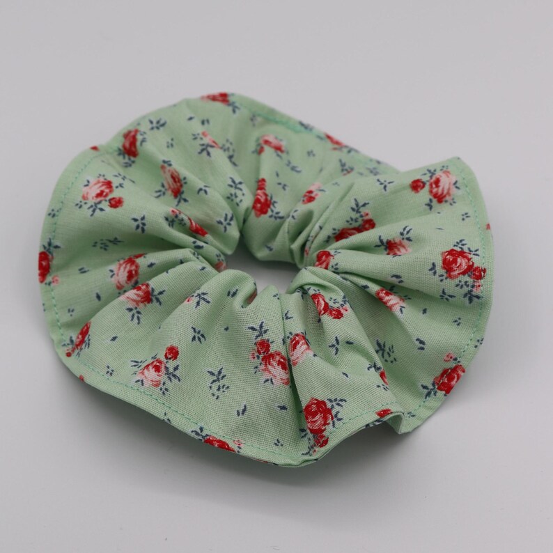 May include: A green fabric scrunchie with a floral pattern featuring red and white roses.