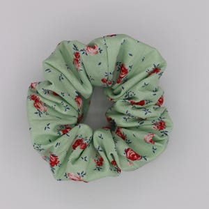 May include: A green scrunchie with a floral pattern featuring red roses and green leaves.