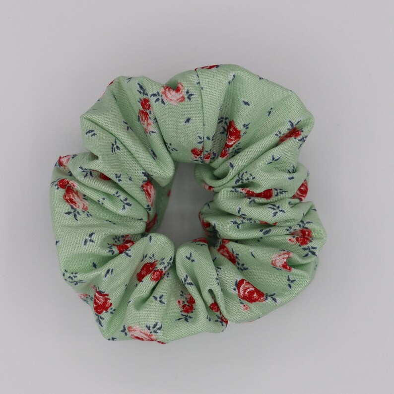 May include: A green scrunchie with a floral pattern featuring red roses and green leaves.