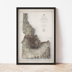May include: Framed vintage map of Idaho in a black frame. The map shows the state's topography in shades of brown and beige, with the title "First Postal Map of Idaho" at the top. The map is detailed and includes place names and geographical features.