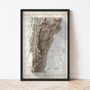 May include: Framed vintage map of Vermont, featuring a 3D topographic relief. The map is in shades of brown and beige, with a black frame. The title "Map of Vermont" is visible.