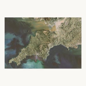 May include: A satellite view of the Cornwall peninsula in England, showing the rugged green and brown terrain of the landmass surrounded by deep blue and turquoise ocean waters, with sediment visible in the coastal areas near the northern shore.