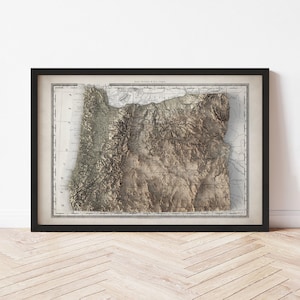 May include: Framed 3D relief map of Oregon, showcasing the state's topography in shades of brown and beige. The map is set within a black frame, offering a vintage aesthetic. The detailed cartography highlights the mountainous regions and geographical features.