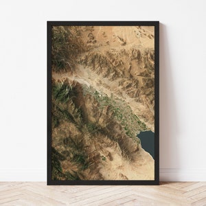 May include: An aerial photograph of a mountainous desert landscape. The image shows a large valley with a river running through it. The mountains are brown and rocky, and the valley is covered in a mix of green vegetation and brown dirt.