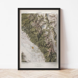 May include: Framed topographic map of a mountainous region, featuring shades of green, brown, and beige. The map is detailed with contour lines and a grid pattern, encased in a black frame. The map is a vintage style.