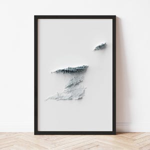 May include: A framed, minimalist art print featuring a 3D topographical map of Trinidad and Tobago. The map is rendered in shades of gray and white, set against a white background, and framed in black. The artwork is displayed on a white wall.