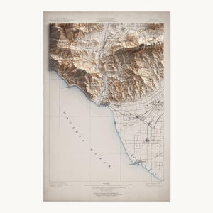 May include: A vintage-style topographic map of Ventura, California, featuring detailed relief shading of mountainous terrain in brown tones alongside a flat coastal plain and the Pacific Ocean. The map includes grid lines and text labels.
