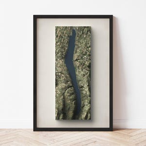 May include: A framed artwork featuring a blue lake surrounded by green land. The artwork is in a black frame and has a white mat.