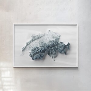 May include: A framed three-dimensional relief map of Switzerland displayed in a white frame. The map features a gradient of white to dark blue, highlighting the rugged topography and mountain ranges of the Swiss landscape in high relief detail.