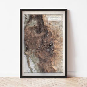May include: Framed topographic map print of the Continental Divide Trail, featuring a detailed relief of the mountain range in shades of brown and beige. The map is set in a black frame, ready for display.