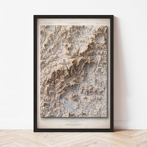 May include: A framed topographic map with a detailed relief of a mountainous region. The map is in shades of brown and beige, with a network of lines representing roads and other features. The frame is black.